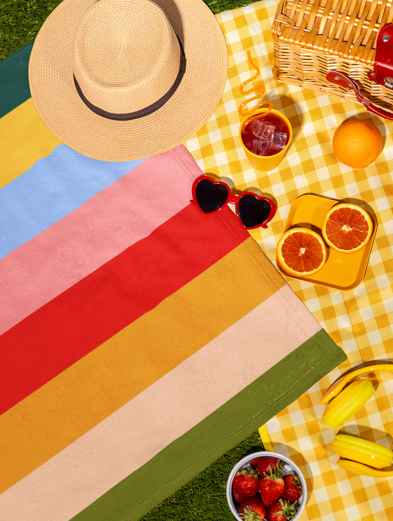 Bold retro stripe towel with summer hat and sunglasses on grass
